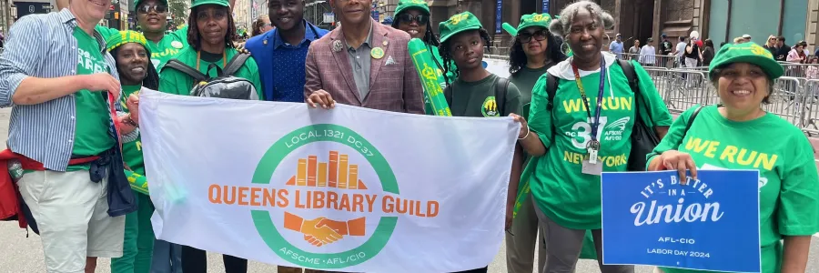 Photo of people holding a Queens Library Guild sign wearing AFSCME Green shirts